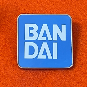 May include: A square, blue pin with the white text "BAN DAI" in a bold, sans-serif font. The pin has a silver border and is set against an orange background.