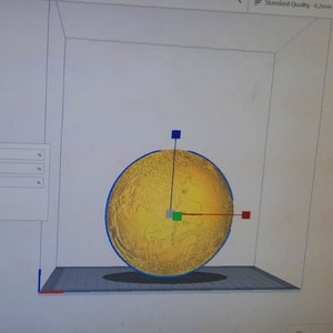 May include: A 3D model of a sphere with a textured surface. The sphere is yellow with a blue outline. The model is positioned on a gray platform with a grid pattern. There are three red, green, and blue squares on the sphere.