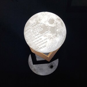 May include: A white moon-shaped night light with a wooden base. The moon has a message engraved on it that reads "To my fiance, I can't find the words to tell you how much you mean to me. I wish I could go back in time and love you longer. My best friend, my favorite person. The love of my life. I wait to spend forever with you. I call you my husband. I love you."