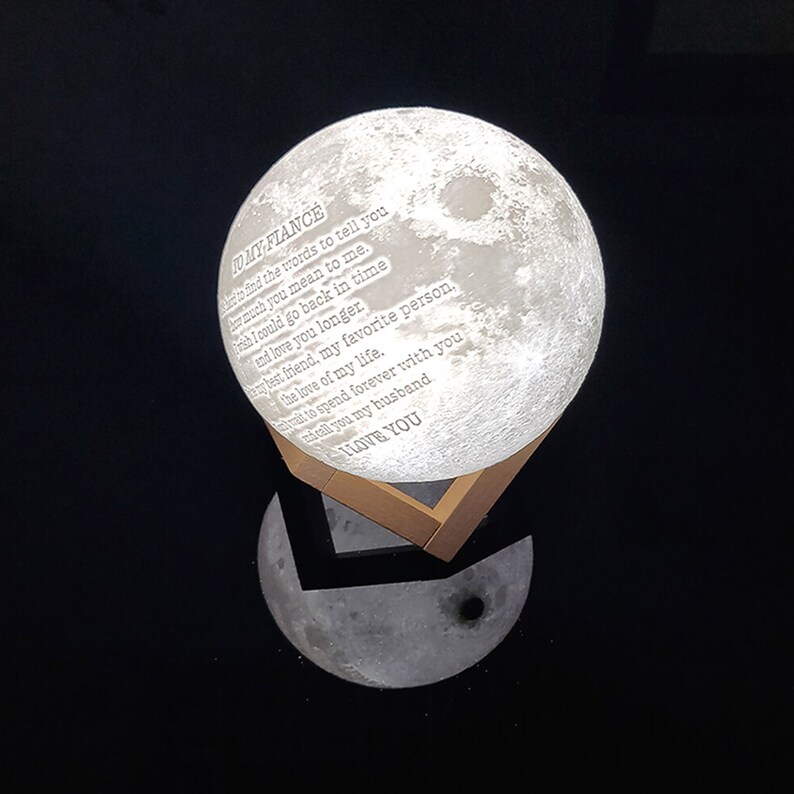 May include: A white moon-shaped night light with a wooden base. The moon has a message engraved on it that reads "To my fiance, I can't find the words to tell you how much you mean to me. I wish I could go back in time and love you longer. My best friend, my favorite person. The love of my life. I wait to spend forever with you. I call you my husband. I love you."