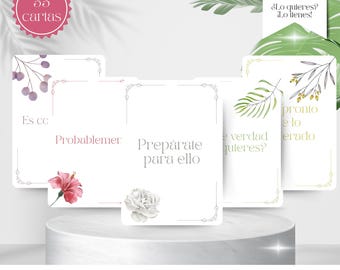 May include: A set of oracle cards with floral accents and text in Spanish. The cards are white with decorative borders and feature phrases like "Prepárate para ello." The image includes a pink flower and a white flower.