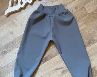 Puede incluir: Pantalones grises para niños pequeños con cintura alta y puños en los tobillos. Los pantalones están hechos de una tela suave y lisa. Un letrero de madera blanca que dice "Love" está en el fondo.