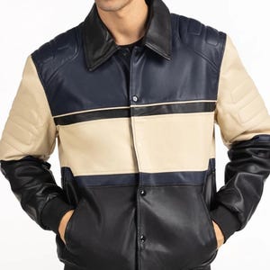 May include: A multi-colored leather jacket with a black collar, navy blue upper section, tan middle section, and black lower section. The jacket has a button-up front, ribbed cuffs, and two front pockets. The brand name "NAMSU" is printed on the lower left.