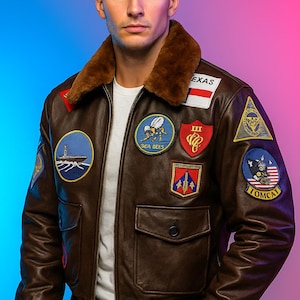 Könnte beinhalten: Braune Leder-Bomberjacke mit mehreren gestickten Aufnähern, darunter "TEXAS", "SEA BEES" und "TOMCAT". Die Jacke hat einen braunen Fellkragen, zwei Vordertaschen und schwarze gerippte Bündchen und Saum.