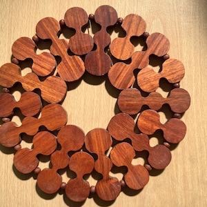 Op de afbeelding: Een ronde houten onderzetter gemaakt van in elkaar grijpende stukken in donkerbruine kleur.