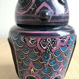 May include: Black ceramic owl-shaped jar with a pink, blue, and white geometric pattern. The jar has a lid and a round body.