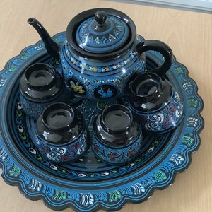 May include: A black tea set with blue and gold painted designs. The set includes a teapot and four cups, all sitting on a black tray with a blue and white patterned border.