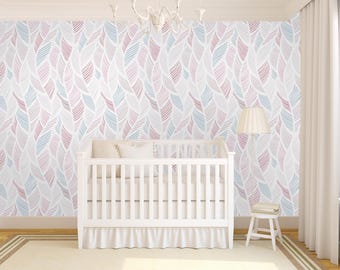 May include: A white crib with a white ruffle skirt sits in front of a white wall with a pink and blue feather pattern wallpaper. A white lamp with a white shade sits on the right side of the crib.