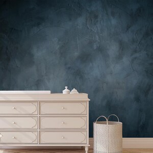 May include: A cream-colored six-drawer dresser with a changing pad and decorative items on top. A woven basket sits on the floor next to the dresser. The background is a dark blue textured wall.