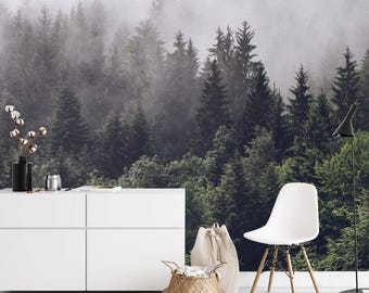 May include: A white dresser with four drawers sits in front of a foggy forest scene wallpaper. A white chair with wooden legs and a woven basket are in the foreground.
