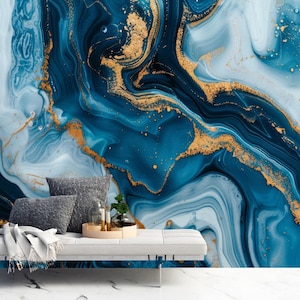 Könnte beinhalten: Ein modernes Wohnzimmer mit einer weißen Bank, grauen Kissen und einer Decke. Der Hintergrund ist eine Wandmalerei mit einem blau-goldenen Marmormuster. Ein Holztablett mit Kerzen und einer kleinen Pflanze steht auf der Bank.
