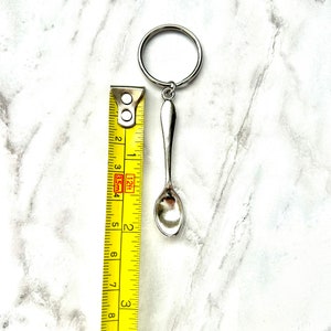 以下が含まれることがあります： リングが付いた銀のスプーンのキーホルダー。スプーンの長さは約5cmで、黄色のメジャーで測定されています。