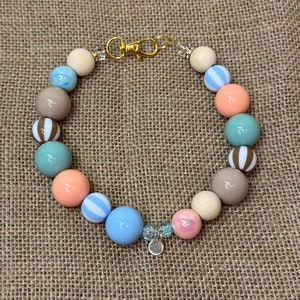 May include: A colorful beaded keychain with a gold clasp. The beads are a mix of light blue, peach, brown, and white. Some beads have stripes and others have a speckled pattern.