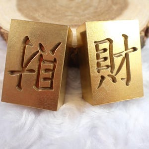 May include: Two gold-colored metal stamps with Chinese characters. The stamp on the left has the character "信" and the stamp on the right has the character "封".