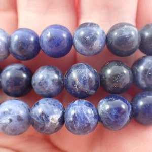May include: Three strands of blue gemstone beads, likely sodalite, are stacked on top of each other. The beads are round and have a slightly mottled appearance.