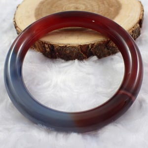May include: A red and blue agate bangle bracelet. The bracelet is made of a smooth, polished stone and has a natural, organic shape.