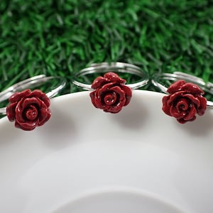 May include: Three silver rings with red rose accents. The rings are on a white plate.