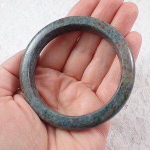 May include: A green and red speckled jade bangle bracelet. The bangle is round and has a smooth, polished finish.