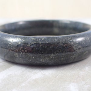 May include: A black bangle bracelet with a speckled pattern of gold pyrite.