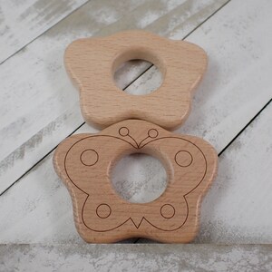 Op de afbeelding: Twee houten bijtringen in de vorm van een ster en een vlinder. Beide bijtringen hebben een gat in het midden dat een baby kan gebruiken om vast te pakken en op te kauwen.