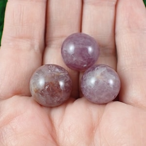 May include: Three smooth, round, purple amethyst spheres. The spheres are polished and have a translucent appearance.