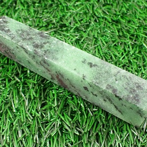 Könnte beinhalten: Ein grüner und schwarzer Edelstein-Stab, auch bekannt als Kristallspitze, auf einem grünen künstlichen Gras-Hintergrund.