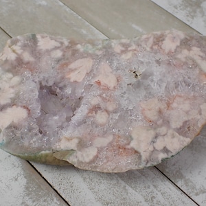 May include: A large, pink and white agate geode with a natural crystal formation. The geode has a rough, irregular shape and is filled with clear quartz crystals.