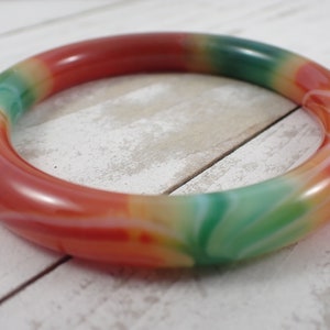 Op de afbeelding: Een kleurrijke armband van rode, groene en witte agaat. De armband is glad en gepolijst, met een draaiende kleurpatroon.