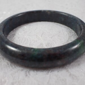 May include: A dark green and black jade bangle bracelet. The bangle is smooth and polished.