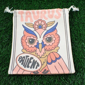May include: A white drawstring bag with a pink owl illustration and the text "Taurus Patient".