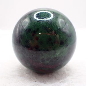Könnte beinhalten: Eine polierte Kugel aus grünem und burgunderfarbenem Stein. Der Orb hat eine glatte, reflektierende Oberfläche mit einem gesprenkelten Muster aus Dunkelgrün und tiefroten Burgundertönen. Die Kugel ist ein dekorativer Gegenstand.