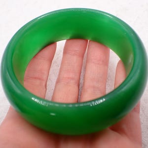 May include: A vibrant green bangle bracelet. The smooth, glossy surface reflects light, highlighting the rich color. The circular design is simple and elegant, suitable for everyday wear. The bangle is approximately 3 inches in diameter.