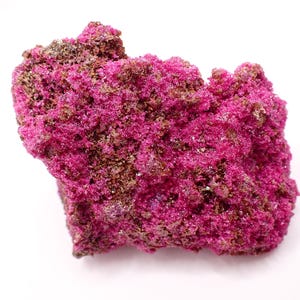 May include: A close-up of a vibrant, crystalline mineral specimen. The mineral features a striking combination of deep magenta and brown hues, with a textured, porous surface. The specimen is set against a clean white background.