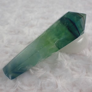 Può includere: Una punta di cristallo di fluorite verde e blu con una punta appuntita e una superficie liscia e lucida.