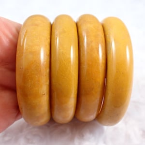 May include: Four yellow plastic bangles stacked together. The bangles are smooth and shiny.