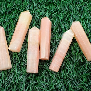May include: Six pink and orange crystal wands on a green artificial grass background.