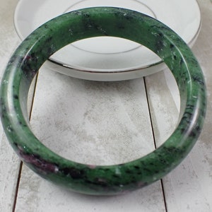 May include: A green and pink jade bangle bracelet. The bracelet is made of a smooth, polished stone with a mottled pattern.