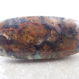 May include: A polished, rectangular slab of agate with a swirling pattern of brown, orange, black, and white. The agate has a smooth, glossy finish.