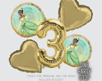 Puede incluir: Un globo de número 3 dorado, dos globos en forma de corazón dorados y dos globos redondos con Tiana de la película de Disney La Princesa y la Rana. Los globos redondos tienen el texto "Dreams are the spice of life".