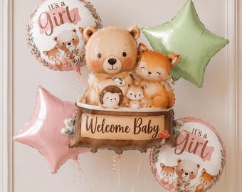 May include: A balloon bouquet featuring a large central balloon shaped like a bear, fox, and hedgehog sitting on a log with the text Welcome Baby. It includes two round balloons with the text It's a Girl, one pink star balloon, and one light green star balloon.