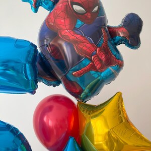 Puede incluir: Un grupo de globos coloridos, que incluyen un globo grande de Spiderman rojo y azul, un globo rojo, un globo de estrella dorada y varios globos azules.