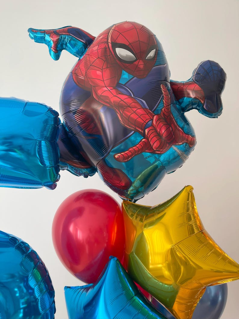Puede incluir: Un grupo de globos coloridos, que incluyen un globo grande de Spiderman rojo y azul, un globo rojo, un globo de estrella dorada y varios globos azules.