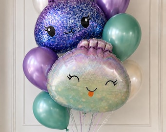 May include: A balloon bouquet featuring two large foil shell-shaped balloons with smiling faces, one in deep purple and one in iridescent teal. These are surrounded by smaller round latex balloons in metallic purple, teal, and white, all tied together.