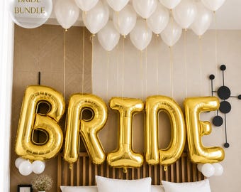 May include: A set of gold foil balloons spelling the word BRIDE, accompanied by a cluster of white latex balloons floating above. The text BRIDE BUNDLE is visible in the upper left corner. The balloons are arranged in a horizontal line.
