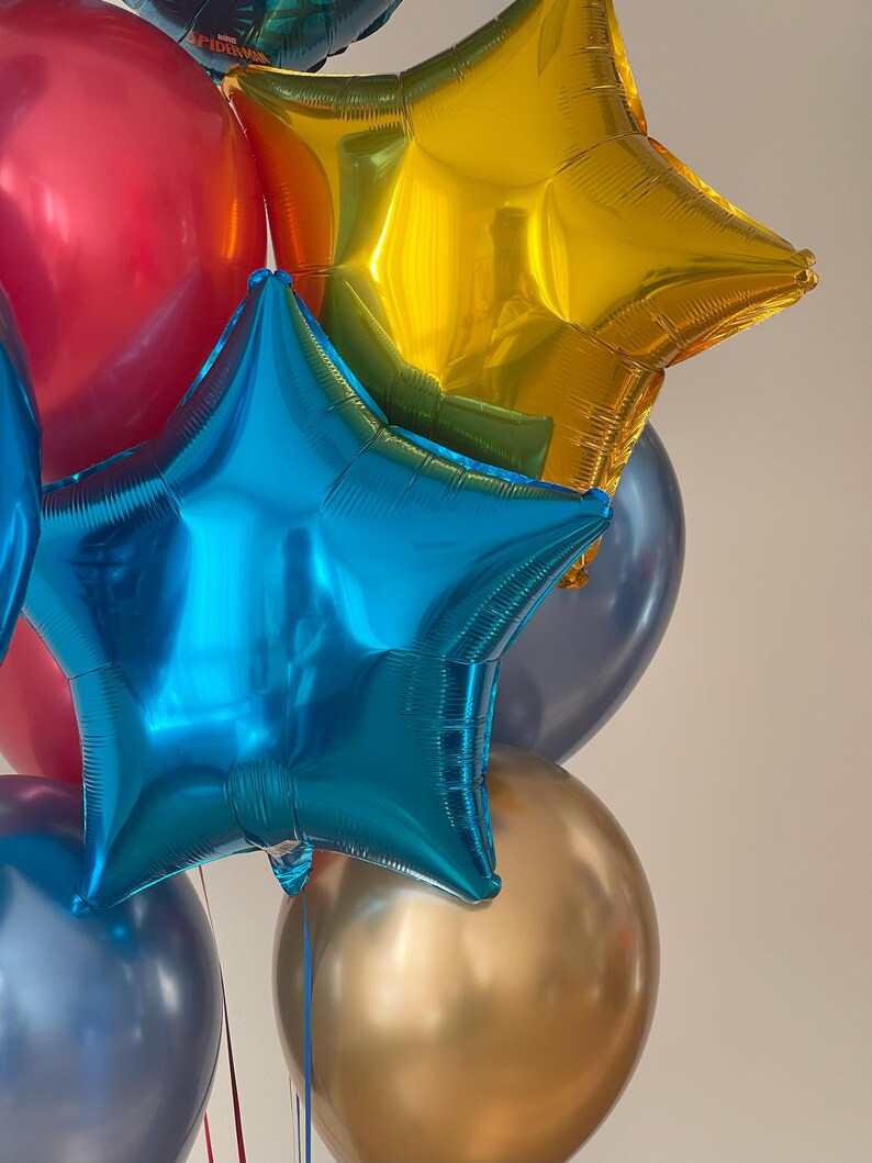 Puede incluir: Un grupo de globos coloridos, que incluyen un globo rojo, un globo azul en forma de estrella, un globo dorado en forma de estrella y un globo dorado.