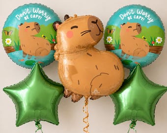 May include: A balloon bouquet featuring two round teal balloons with a capybara illustration and the text Don't Worry Be Capy, one large tan capybara-shaped balloon, and two solid green star-shaped balloons, all with attached curling ribbons.
