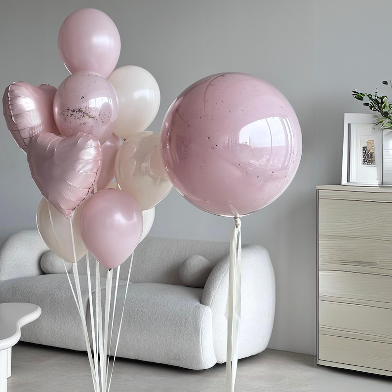 May include: A collection of pink and white balloons, including heart-shaped and round designs. Some balloons have glitter accents. The balloons are tied with white ribbons, creating a festive and celebratory display.