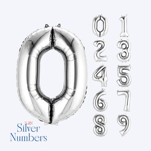 May include: Silver number balloons in various shapes, including the number zero. The balloons are silver and shiny, with a metallic finish. The text "34-IN Silver Numbers" is printed in a script font. These balloons are suitable for birthdays and other celebrations.