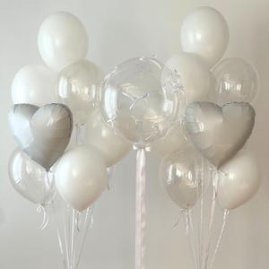 May include: A bouquet of white and clear balloons, including two heart-shaped balloons, with a large clear bubble balloon in the center.