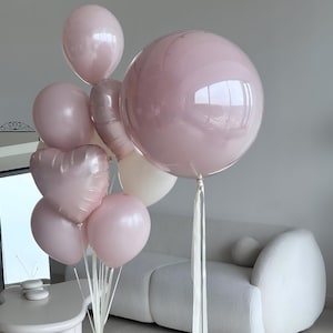 May include: A collection of pink balloons, including round and heart-shaped designs, with white ribbons. The balloons vary in size and shade, creating a soft, celebratory aesthetic. Some balloons have a glittery appearance.